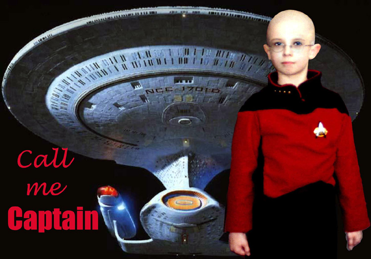 A child sized Captain Picard poses in front of the TNG Starship Enterprise